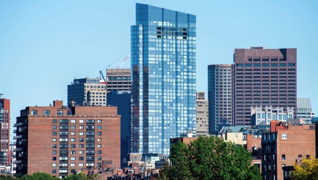 Paisaje urbano que destaca un moderno rascacielos acristalado con el distintivo logotipo de CBRE en su fachada principal, posicionado estratégicamente en el centro de la escena. El edificio se impone entre elegantes construcciones históricas de ladrillo, creando un contraste arquitectónico sofisticado. La presencia de áreas verdes cuidadosamente integradas y la claridad del cielo enfatizan la exclusividad y el dinamismo característico de los distritos inmobiliarios más cotizados, consolidando este enclave como una referencia imprescindible para inversores o compradores que buscan calidad, rentabilidad y prestigio en ubicaciones prime.