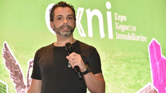 Un profesional del sector inmobiliario premium, identificado por su estilo contemporáneo y presencia segura, toma la palabra frente a un gran panel digital que exhibe el nombre “Expo Negocios Inmobiliarios”. En su intervención, subraya la importancia de crear ecosistemas integrales pensados para aportar valor a cada uno de los actores clave en el mercado. Su mensaje reitera el compromiso con la innovación y la excelencia, atributos esenciales para inversores y compradores exigentes que buscan participar en entornos inmobiliarios exclusivos y sostenibles.