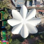 Vista aérea de Los Manantiales, una imponente edificación blanca reconocida por su emblemático techo en forma de flor. Ubicado en un entorno arbolado y rodeado de infraestructura urbana, este inmueble destaca como una exclusiva joya arquitectónica. Sus líneas únicas y su integración con el paisaje hacen de Los Manantiales una propiedad icónica, ideal para inversores que buscan activos premium con elevado potencial de valorización dentro del sector inmobiliario más selecto.