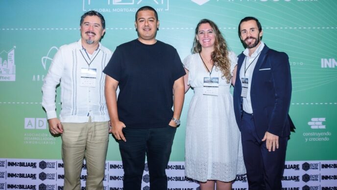 Cuatro profesionales se posan juntos frente a un elegante fondo de evento decorado con logotipos exclusivos y una estética que evoca el estilo cómodo de Tulum. Tres de ellos visten atuendos ejecutivos, reflejando el estándar del sector inmobiliario premium, mientras que uno apuesta por un look contemporáneo con camiseta negra y pantalón beige. Todos portarán acreditaciones oficiales del evento, evidenciando su participación activa en entornos selectos dedicados a la inversión y adquisición de propiedades de alto nivel.