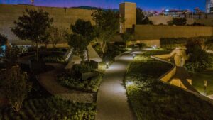 Vista nocturna de los exclusivos jardines paisajísticos de Origina Pedregal, donde senderos iluminados realzan la vegetación selecta y las elegantes estructuras arquitectónicas. El diseño integra muros de concreto contemporáneo y enmarca una perspectiva privilegiada hacia el horizonte urbano, ofreciendo una atmósfera distinguida ideal para quienes buscan un entorno residencial de alto nivel e inversión inmobiliaria premium.