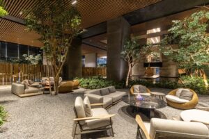 Exclusiva área lounge al aire libre en Origina Pedregal, diseñada para los estilos de vida más atractivos. Este elegante espacio destaca por su mobiliario de alta gama en fibras naturales, asientos acolchados y una imponente fogata central que invita a momentos inolvidables. Rodeado de árboles maduros y vegetación exuberante, cuenta con piso de gravilla selecta y techo con listones de madera para un ambiente contemporáneo. La iluminación cálida resalta cada detalle arquitectónico y natural, creando un entorno ideal tanto para la relajación privada como para el entretenimiento social exclusivo. Una propuesta única que fusiona naturaleza, diseño moderno y confort premium; atributos esenciales para inversionistas o compradores que buscan la máxima calidad en el sector inmobiliario residencial de alto nivel.