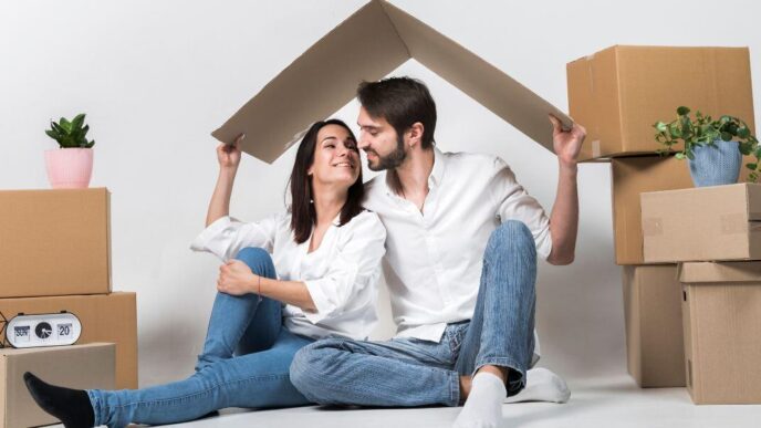 Una pareja celebra la adquisición de su nuevo hogar, rodeado de cajas de mudanza y detalles naturales que realzan el ambiente exclusivo de su residencia. Gracias al acceso a soluciones crediticias personalizadas, han hecho realidad su inversión en una propiedad premium. Juntos sostienen sobre sus cabezas una figura en forma de techo, símbolo del inicio de una nueva etapa marcada por seguridad, confianza y visión patrimonial en el sector inmobiliario de alta gama.