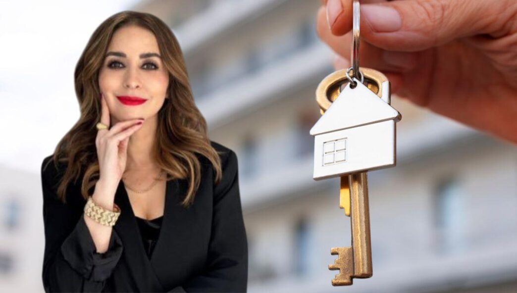 Una mujer elegantemente vestida en negro posa con confianza, transmitiendo sofisticación frente a un moderno edificio difuminado al fondo. En primer plano, una mano sostiene una llave con un llavero en forma de casa, símbolo de acceso exclusivo al mercado residencial premium en México. Esta imagen representa las oportunidades excepcionales de inversión y adquisición inmobiliaria para quienes buscan propiedades distintivas y exclusivas en los destinos más prestigiosos del país.