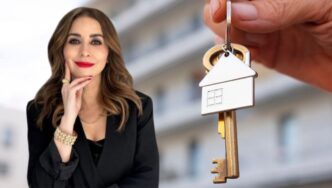 Una mujer elegantemente vestida en negro posa con confianza, transmitiendo sofisticación frente a un moderno edificio difuminado al fondo. En primer plano, una mano sostiene una llave con un llavero en forma de casa, símbolo de acceso exclusivo al mercado residencial premium en México. Esta imagen representa las oportunidades excepcionales de inversión y adquisición inmobiliaria para quienes buscan propiedades distintivas y exclusivas en los destinos más prestigiosos del país.