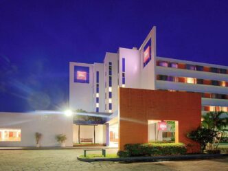 Edificio hotelero de múltiples niveles gestionado por Accor, con la reconocida insignia ibis en su fachada, destacado por su diseño moderno e iluminación arquitectónica nocturna que resalta su presencia urbana. La entrada principal, marcada por una elegante estructura naranja y rodeada de jardín cuidadosamente seleccionada, ofrece una bienvenida sofisticada y exclusiva. Esta propiedad representa una oportunidad excepcional para inversores o compradores que buscan activos inmobiliarios premium en el sector hotelero internacional.