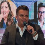 Un ejecutivo de alto nivel se dirige al público en un evento de proptech, transmitiendo su visión sobre las tendencias que están definiendo el futuro del sector inmobiliario premium. En la pantalla detrás de él, se exhiben los nombres y retratos parciales de destacados referentes, subrayando el exclusivismo y la relevancia del encuentro. Este escenario reúne a inversores y compradores exigentes interesados en oportunidades innovadoras, tecnología avanzada y alianzas estratégicas que elevan los estándares del mercado de bienes raíces de lujo.