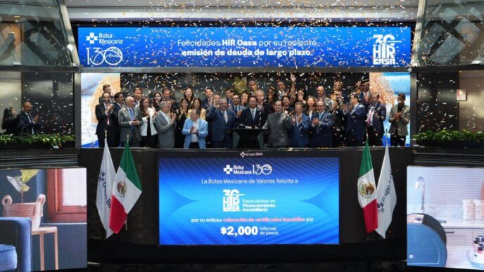 Un selecto grupo de profesionales del sector inmobiliario, elegantemente vestidos, se reúne en el escenario principal de la Bolsa Mexicana de Valores para celebrar un hito estratégico de HIR CASA. Flanqueados por dos banderas nacionales y bajo una lluvia de confeti, los líderes y socios clave comparten este momento trascendental mientras una pantalla proyecta mensajes de reconocimiento e información financiera relevante. Este evento simboliza la solidez, prestigio y proyección internacional que distingue a HIR CASA en el mercado inmobiliario premium, confirmando su atractivo incomparable para inversionistas acreedores y compradores exigentes que buscan oportunidades exclusivas con visión a futuro.