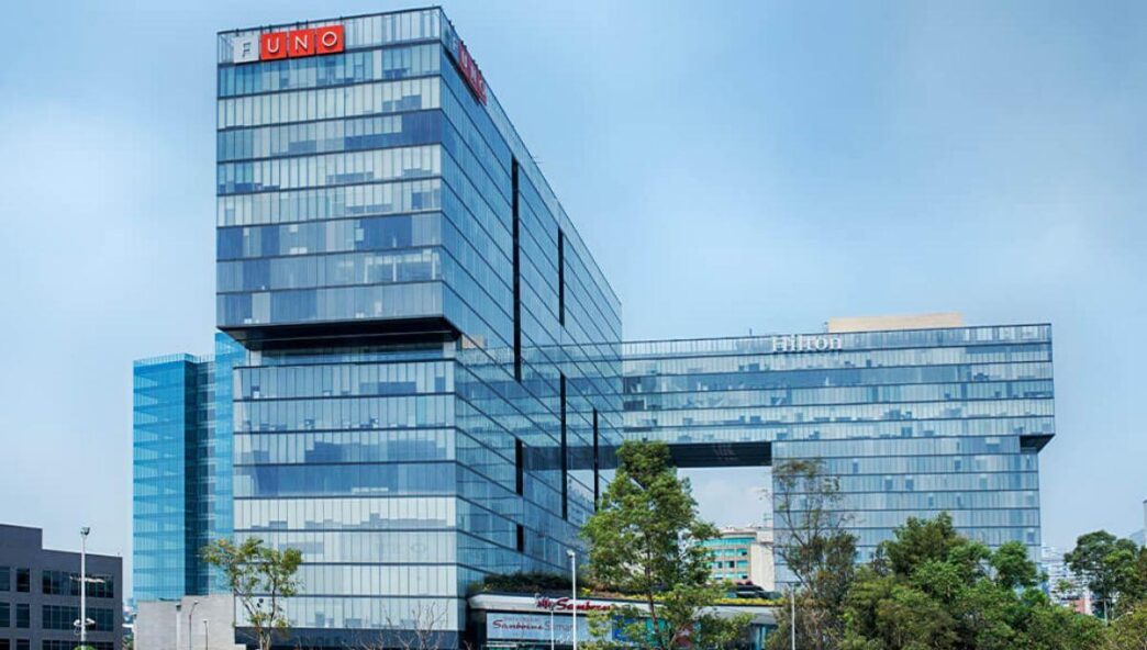 Edificio corporativo de vanguardia, desarrollado en varios niveles con una impresionante fachada de vidrio y un innovador diseño geométrico. Alberga reconoce firmas internacionales como UNO, Hilton y FUNO, lo que garantiza un entorno empresarial exclusivo y de alto perfil. Rodeado de áreas verdes cuidadosamente integradas al paisaje urbano y situado bajo un cielo despejado, este inmueble representa una oportunidad inigualable en el sector inmobiliario premium para inversionistas y empresas que buscan distinción, prestigio y plusvalía garantizada.