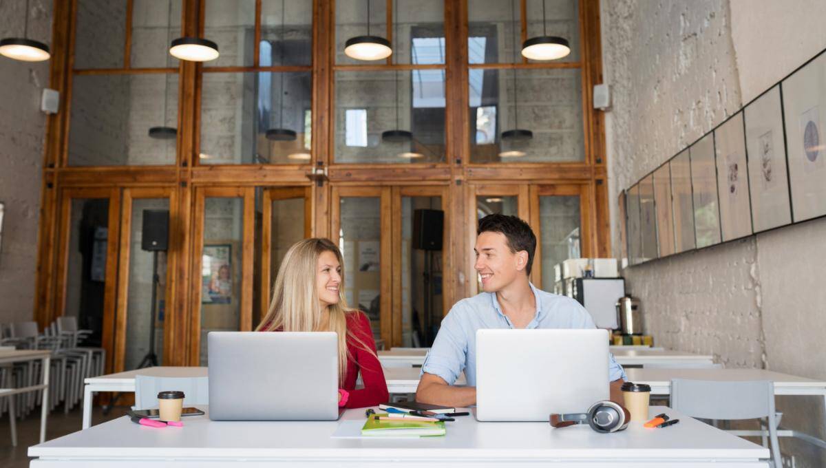 Dos profesionales ocupan una mesa en oficinas de diseño contemporáneo, caracterizadas por ventanas de gran altura y elegantes marcos de madera. El ambiente, cuidadosamente concebido para potenciar la productividad y fomentar la colaboración, representa un entorno ideal para inversores y compradores que valoran espacios empresariales exclusivos, funcionales y a la vanguardia del sector inmobiliario premium.