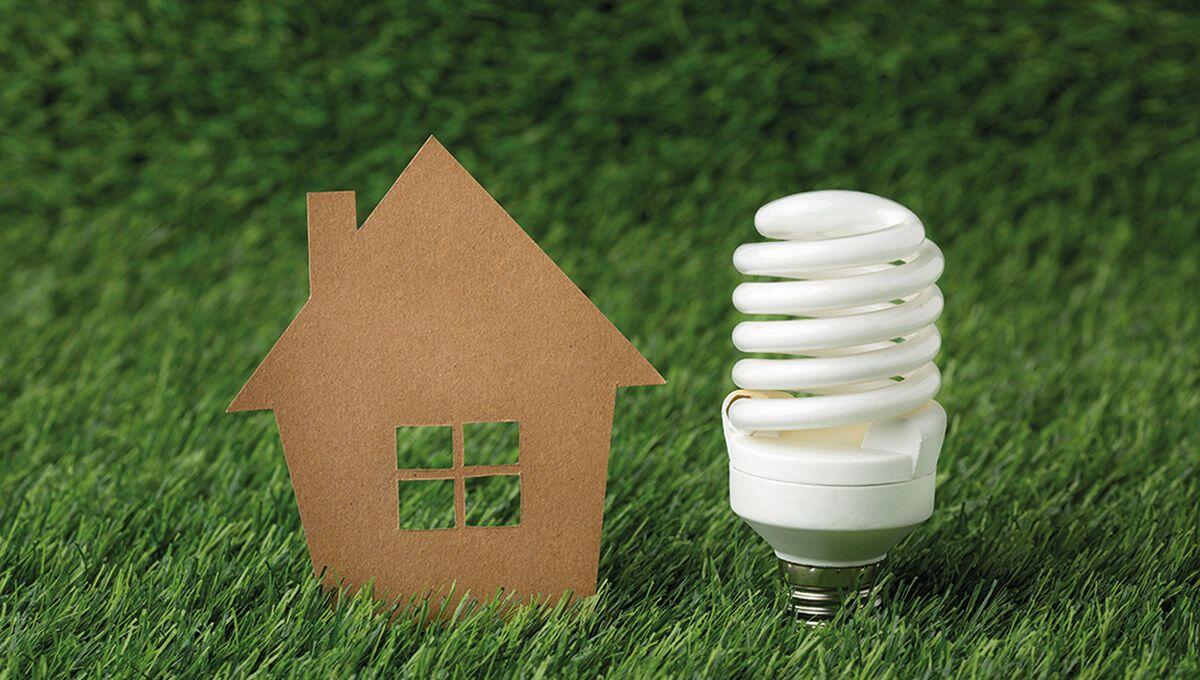 Un recorte representativo de una vivienda y una lámpara de bajo consumo se sitúan sobre césped natural, evocando el concepto de vivienda sustentable. Esta imagen transmite un firme compromiso con la eficiencia energética y la responsabilidad ambiental, elementos esenciales en el segmento inmobiliario premium para inversores y compradores que priorizan la innovación, la sostenibilidad y el valor a largo plazo.