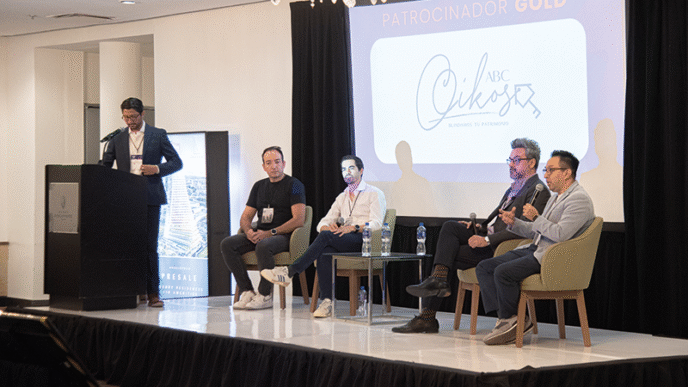 Cinco destacados profesionales del sector lideran un panel enfocado en innovación proptech y digitalización inmobiliaria, abordando tendencias clave que transforman el mercado premium. Un ponente principal expone desde el podio, mientras cuatro expertos debaten con micrófono en mano, aportando perspectivas estratégicas para inversores y compradores de alto perfil. De fondo, la pantalla resalta el patrocinio Gold y exhibe con distinción la marca ABC Cikos, subrayando la exclusividad y relevancia del evento.