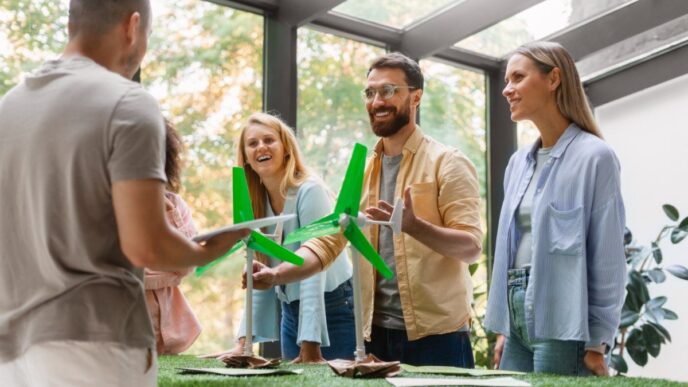Un grupo de cuatro adultos se reúne en torno a una mesa que exhibe maquetas de aerogeneradores, en un entorno interior luminoso y moderno. Mientras uno de los asistentes sostiene documentación relevante, los demás interactúan y analizan activamente el potencial de las energías renovables como valor añadido para desarrollos inmobiliarios sostenibles. El espacio cuenta con amplios ventanales que permiten la entrada de luz natural y ofrecen vistas despejadas hacia áreas arboladas, aportando una atmósfera exclusiva que integra innovación, responsabilidad ambiental y máxima calidad en la experiencia residencial o inversora.