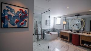 Baño moderno de diseño exclusivo, equipado con una ducha espaciosa cerrada en cristal, bañera independiente de inspiración contemporánea y doble lavabo sobre una elegante encimera, rematado por un cómodo espejo circular. Destacan los acabados premium en mármol y la presencia de arte abstracto en tonos azul y rojo, generando un ambiente refinado al estilo boutique característico de los Hoteles Pueblo Bonito. Un espacio que eleva el estándar residencial e incrementa el valor patrimonial para clientes e inversores que buscan lo mejor del sector inmobiliario premium.