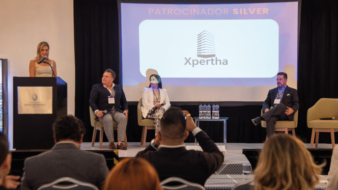 En el marco del exclusivo congreso REBS Puebla, cuatro destacados profesionales del sector inmobiliario se presentan en el escenario: uno de ellos lidera la conversación desde el podio, mientras los otros tres expertos acompañan la sesión como panelistas. En una pantalla principal se exhibe el logotipo de Xpertha junto a la distinción de "Patrocinador Silver", subrayando su compromiso con la excelencia y la innovación en bienes raíces premium. Ante una audiencia selecta y atenta, se exponen atractivas oportunidades de inversión diseñadas para satisfacer las expectativas de inversores visionarios y compradores exigentes en busca de proyectos inmobiliarios exclusivos y altamente rentables.