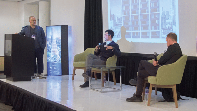 Tres destacados expertos del sector participaron en un panel sobre Innovación en Arquitectura, enfocado en el desarrollo de espacios urbanos excepcionales. Uno de los ponentes lideró la presentación desde el podio, mientras que los otros dos compartieron sus perspectivas desde el escenario, cada uno con micrófono. Una proyección de un edificio icónico ilustró la discusión, resaltando las tendencias actuales y las oportunidades exclusivas que ofrece la arquitectura de vanguardia para inversores y compradores inmobiliarios premium que buscan activos distintivos en entornos urbanos privilegiados.