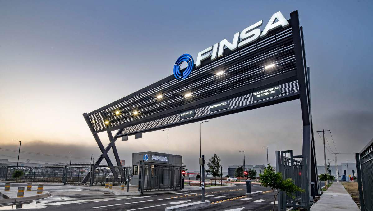 Acceso principal a parque industrial de alta gama, con un imponente letrero negro FINSA iluminado, caseta de seguridad equipada, barreras automáticas y vialidades completamente pavimentadas. Esta infraestructura moderna refleja los más altos estándares inmobiliarios para 2024 y subraya el compromiso con la Certificación LEED, garantizando eficiencia, sostenibilidad y máxima seguridad para inversionistas y compradores que exigen excelencia.
