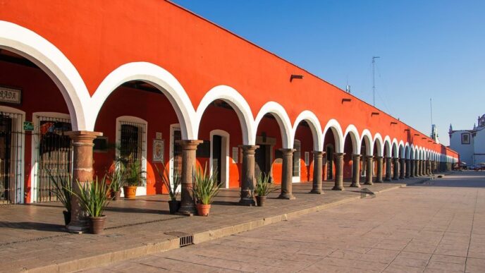 Una elegante hilera de arcos blancos, sostenidos por sólidas columnas en tonos marrones, realza la fachada de esta exclusiva propiedad de color rojo intenso en Puebla, bajo un cielo azul inmaculado. El pasillo se embellece con plantas ornamentales dispuestas estratégicamente y un piso de piedra cuidadosamente colocado, que resalta la autenticidad y el atractivo arquitectónico tradicional. Esta combinación única ofrece una oportunidad inigualable para inversores o compradores que buscan adquirir un inmueble premium con gran valor estético, ubicación privilegiada y potencial para usos residenciales o comerciales exclusivos.