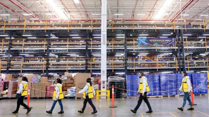 Trabajadores en almacén mexicano reflejan inversión privada en México. Amplio espacio con estanterías llenas y personal con chalecos de seguridad.