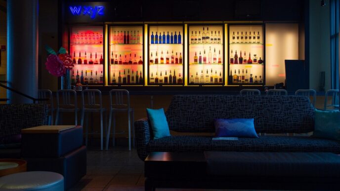 Elegante bar con licores iluminados, sofás modernos y sillas altas. Ambiente nocturno y relajante con decoración cuidada y luces de neón.