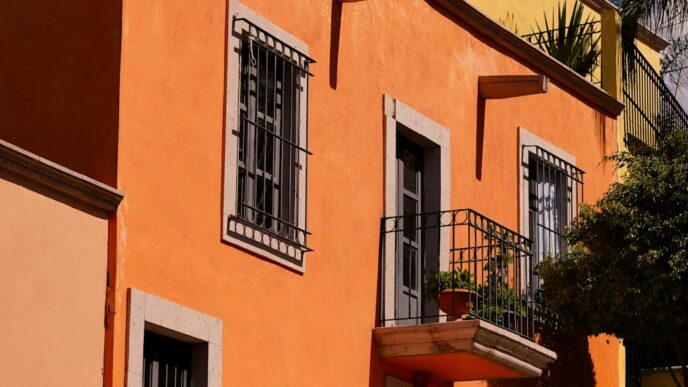 Fachada colorida en San Miguel de Allende, México, con balcones de hierro forjado y ventanas enrejadas bajo un cielo azul vibrante. Arquitectura colonial.