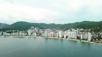 Vista aérea de Acapulco, México, mostrando la costa con edificios altos, montañas verdes y el océano. Destino turístico popular de México.