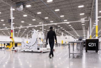 Interior de la futura planta de Archer para fabricación aeronáutica en 2024, mostrando equipos de ensamblaje y un empleado caminando. Espacio amplio.