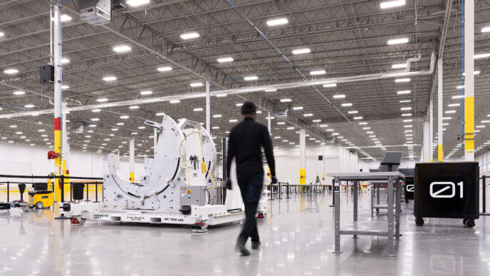 Interior de la futura planta de Archer para fabricación aeronáutica en 2024, mostrando equipos de ensamblaje y un empleado caminando. Espacio amplio.