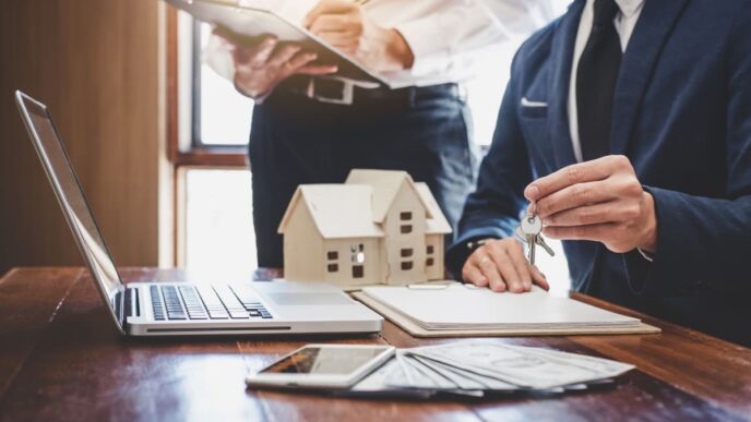 Asesores inmobiliarios digitalizados mostrando llaves de una casa. Laptop, dinero y contratos sobre la mesa. Firma de documentos.