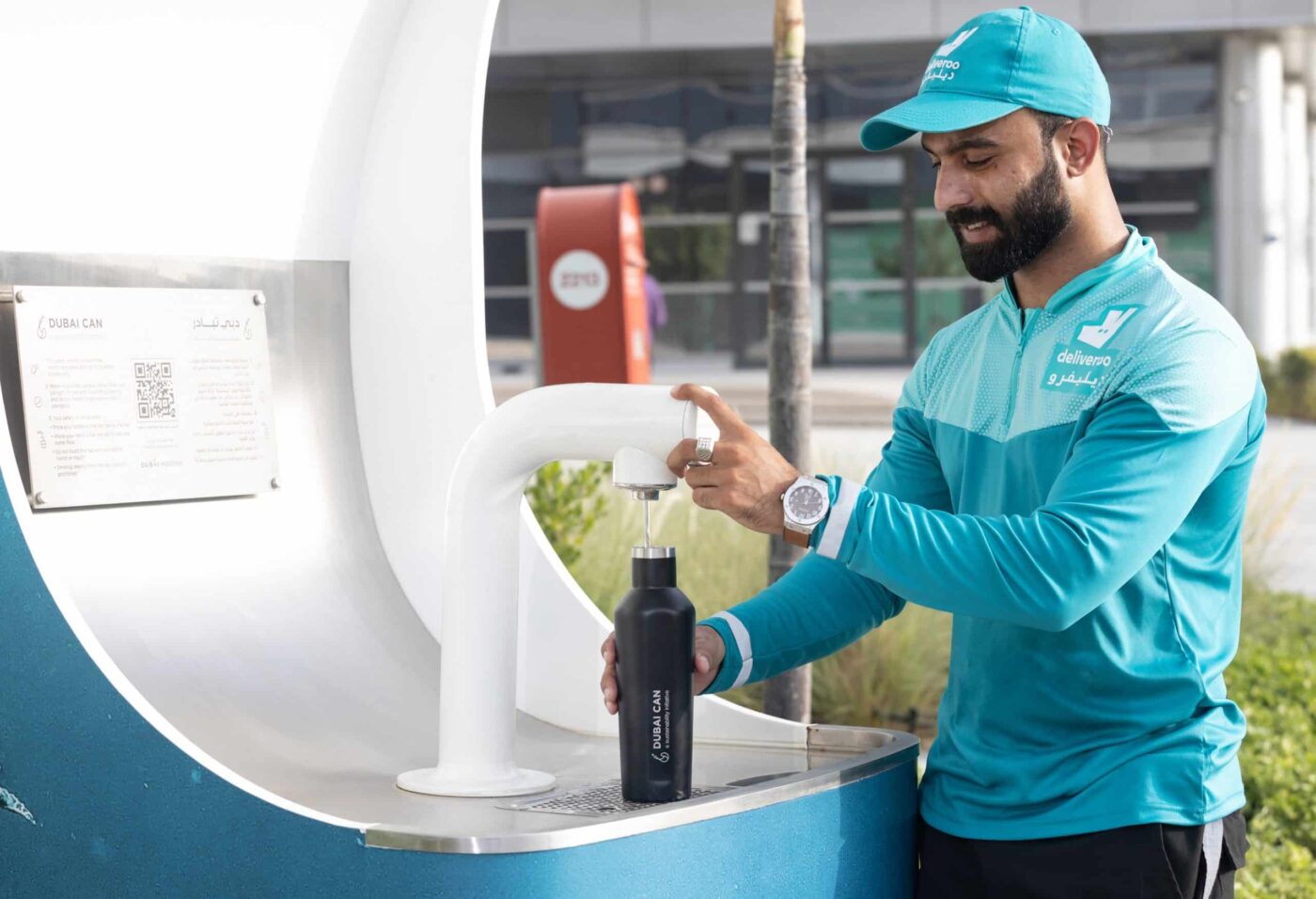 Hombre de Deliveroo rellena botella reutilizable en fuente Dubai Can. Iniciativa para reducir plástico, como ATELIER de Hoteles promueve.