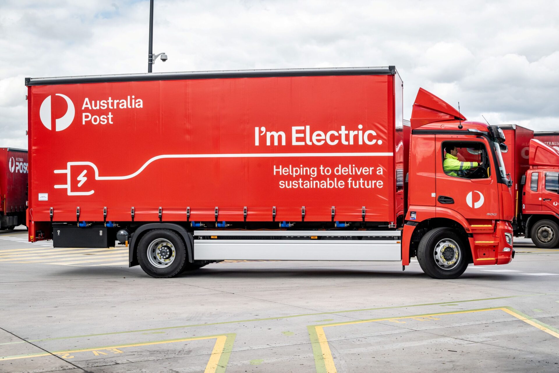 Australia Post electric delivery truck, red with "I'm Electric" and plug graphic, part of sustainable fleet initiative. Boosting cleaner transport.