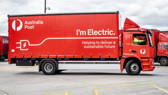Australia Post electric delivery truck, red with "I'm Electric" and plug graphic, part of sustainable fleet initiative. Boosting cleaner transport.