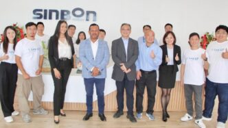 Grupo en la planta de Automann en SLP celebrando el avance de la construcción. Empleados y directivos posan frente al logo de Sinbon, mostrando su apoyo.