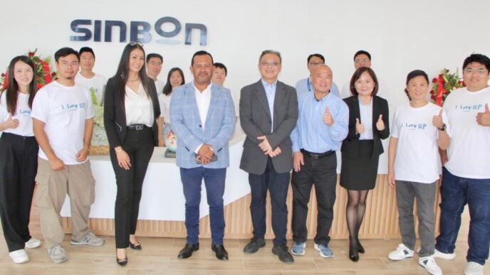 Grupo en la planta de Automann en SLP celebrando el avance de la construcción. Empleados y directivos posan frente al logo de Sinbon, mostrando su apoyo.