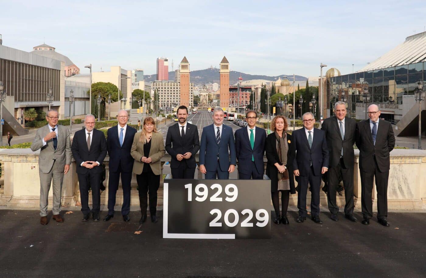Grupo posa en Montjuïc, Barcelona, para la renovación del recinto. Inversión de 174 mde, torres gemelas al fondo. Anuncio de 1929-2029.