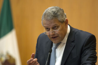 Primer plano de directivo de BBVA México anunciando créditos hipotecarios. Bandera mexicana al fondo. Apoyo a la vivienda en el país.