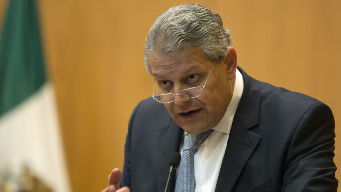 Primer plano de directivo de BBVA México anunciando créditos hipotecarios. Bandera mexicana al fondo. Apoyo a la vivienda en el país.