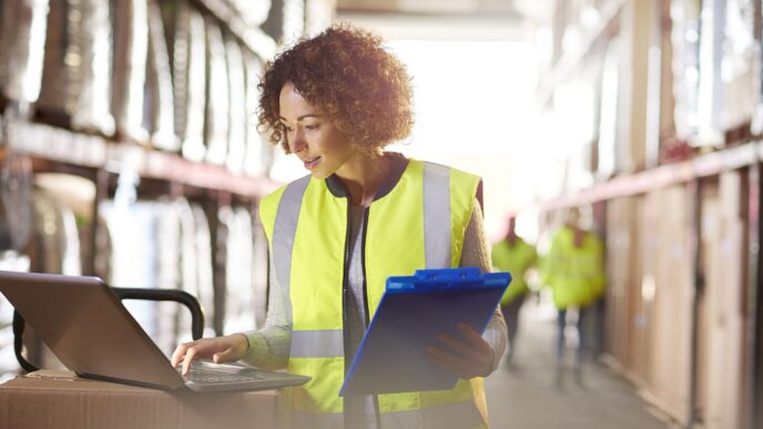 networking/expo
Mujer con chaleco de seguridad usando laptop y portapapeles en almacén. Gestión de inventario y logística.