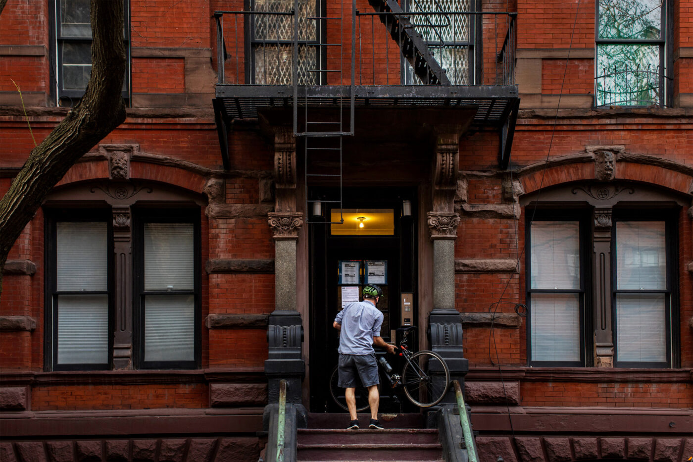 Fachada de edificio de ladrillo en Nueva York, con un hombre subiendo las escaleras con una bicicleta. Impacto inmobiliario y leyes de vivienda.