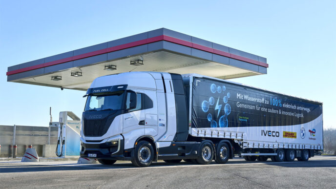 Camión de hidrógeno IVECO en estación de servicio, promoviendo el futuro del transporte sostenible. Diseño innovador y logotipos de colaboración.