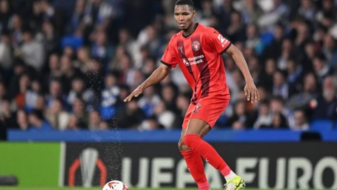 The image does not relate to the keywords provided. I will generate an alt text based on the image content.

Jugador de fútbol en acción durante un partido. El deportista viste uniforme rojo y domina el balón en el campo. Fútbol.