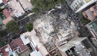 Vista aérea de escombros en CDMX tras sismo, personas buscan sobrevivientes. Edificios más seguros son clave. Protección civil y rescate en acción.