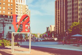 Escultura LOVE roja y verde en Filadelfia, con edificios altos al fondo. Atractivo turístico en un día soleado, ideal para fotos y recuerdos.