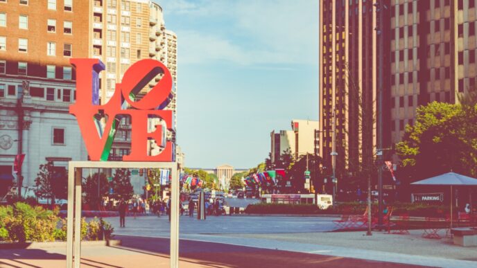 Escultura LOVE roja y verde en Filadelfia, con edificios altos al fondo. Atractivo turístico en un día soleado, ideal para fotos y recuerdos.