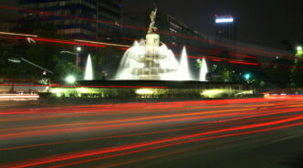 Fuente de Diana Cazadora en Ciudad de México, capturada con larga exposición que muestra estelas de luz de tráfico nocturno. 125 caracteres
