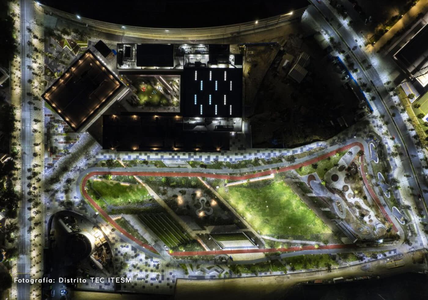 Vista aérea nocturna del Distrito TEC ITESM en Ciudad Juárez. Espacios verdes, edificios iluminados y senderos resaltan el desarrollo urbano sostenible.
