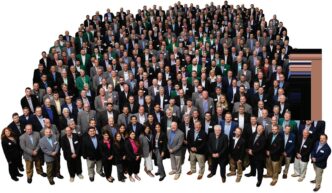 Gran grupo de personas vestidas formalmente, posiblemente asociadas con Clio Asset Management y Builders FirstSource, reunidas para una foto grupal.