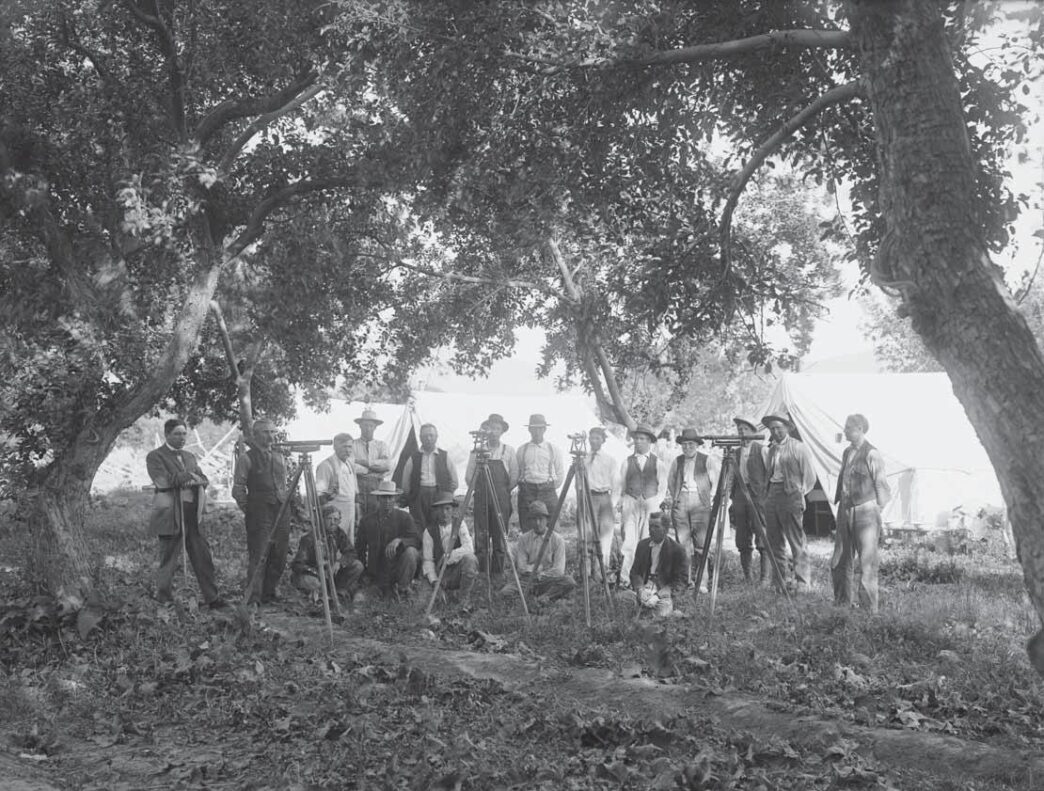 Category: venue/architecture
Grupo de hombres con equipos de topografía al aire libre, posiblemente en México. Arquitectura histórica en blanco y negro.