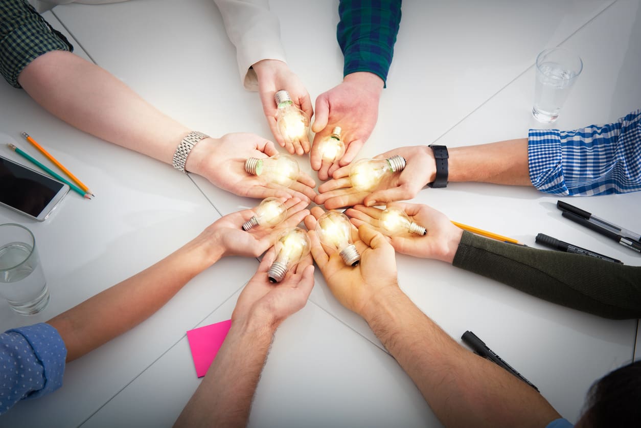 Grupo de personas sosteniendo bombillas en una mesa, simbolizando ideas en un evento Inmobiliare Summits. Coworking y real estate en México.