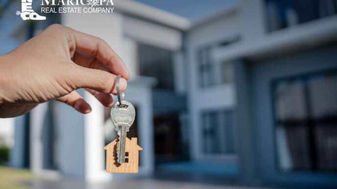 Llaves de nueva oferta inmobiliaria 2022. Mano sosteniendo llave con llavero de casa frente a una vivienda moderna. Colocación inmobiliaria.